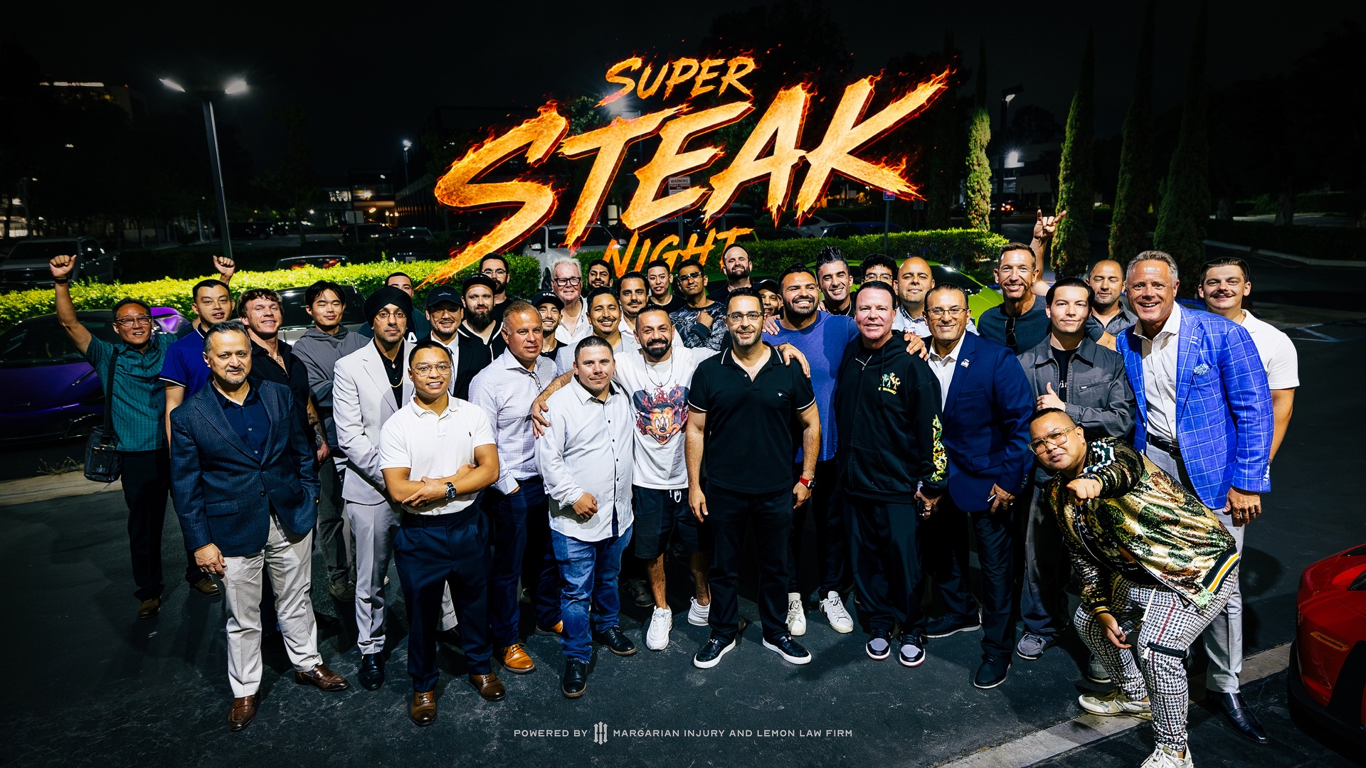 Super Steak Night group photo: Hovanes Margarian with dinner guests at night, under a flaming Super Steak Night title